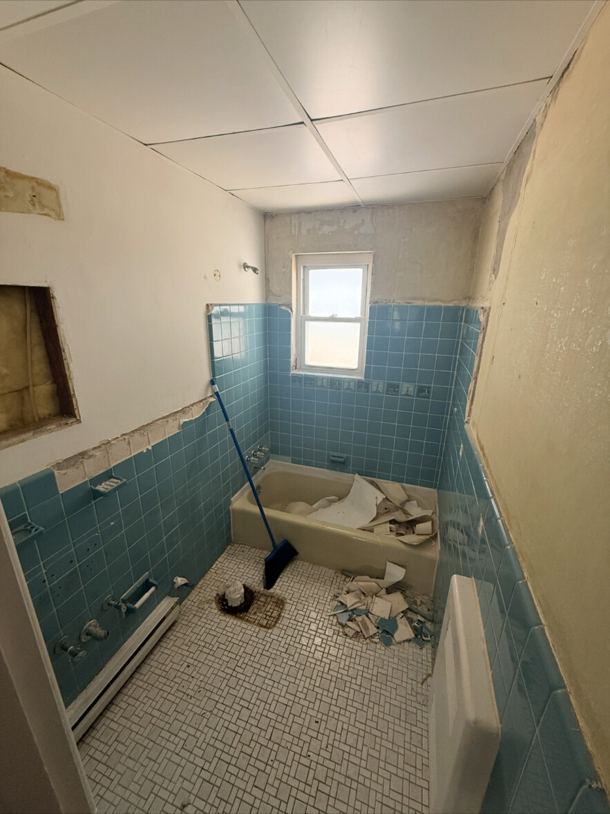 Bathroom gutted to old blue tile, tub and torn-up walls during demolition
